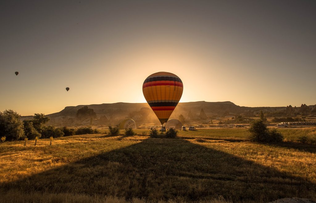 A picture of a colorful hot air balloon in a field surrounded by greenery and mountains during sunset Wildlife Safari Adventure