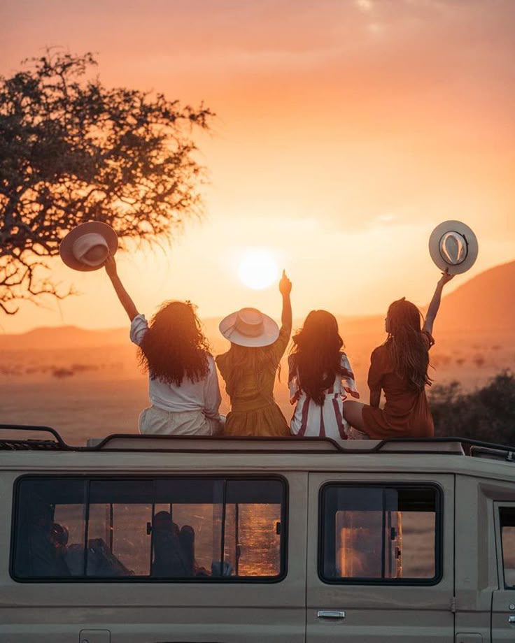 A group of travelers sitting on top of an open-roof 4x4 vehicle cheering at sunset during an affordable group safari Kenya tour package.